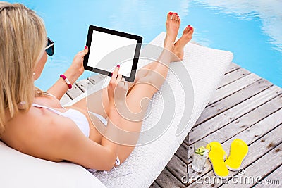 Woman using tablet computer while sunbathing in chair by the pool Stock Photo