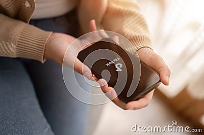 A woman using TikTok application on an IPhone14 while relaxing indoors. A TikTok logo on an IPhone14 Editorial Stock Photo