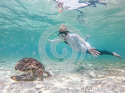 Woman on vacations wearing snokeling mask swimming with sea turtle in turquoise blue water of Gili islands, Indonesia Stock Photo