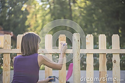 Woman varnishing a wooden picket fence Stock Photo