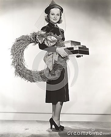 Woman in veiled hat carrying wreath and Christmas presents Stock Photo