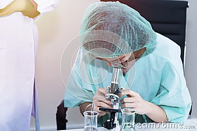 Woman veterinary student looking through a microscope near test tube Stock Photo