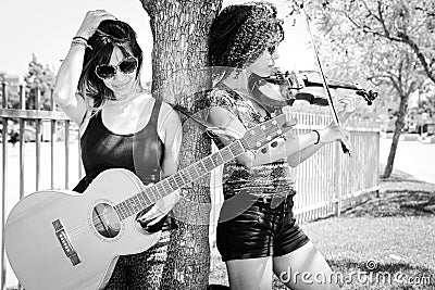 Woman violinist and woman guitarist leaning against tree Stock Photo