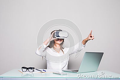 Woman in VR glasses. Confident young woman in virtual reality headset pointing in the air while sitting at her working place in of Stock Photo