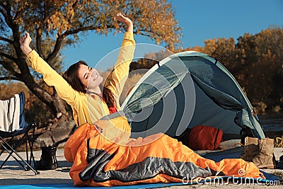 Woman waking up in sleeping bag near tent Stock Photo