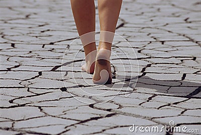 Woman walking barefoot across cracked earth Stock Photo