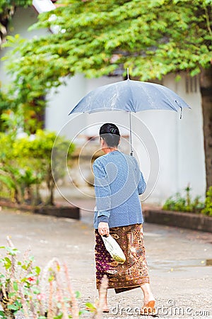 Woman walking down the street under an umbrella in Louangphabang, Laos. Vertical. Editorial Stock Photo