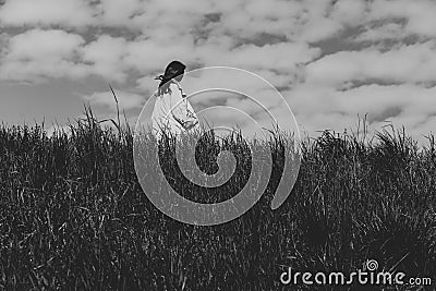 Woman walking in the tall grass on a windy day, alone, keeping distance from people Stock Photo