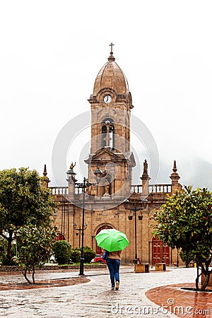 Woman walking with an umbrella at the beautiful central square aof the small town of Nobsa in a rainy day Stock Photo