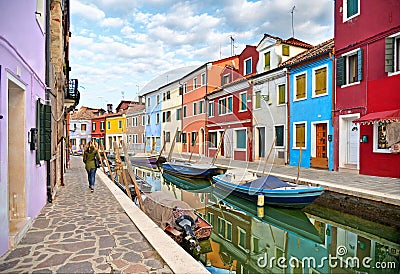 Woman walks in Burano island picturesque street with small colored houses in row, water canal with fishermans boats, c Editorial Stock Photo