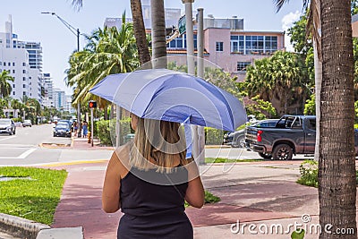 Woman walks down street, shielding herself from scorching sun with UV-protective umbrella. Stock Photo