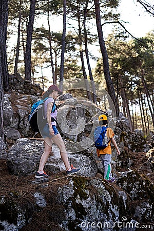 A woman walks with her son through the forest, The boy with his mother go hiking, A child with a backpack is in the park, Travel Stock Photo