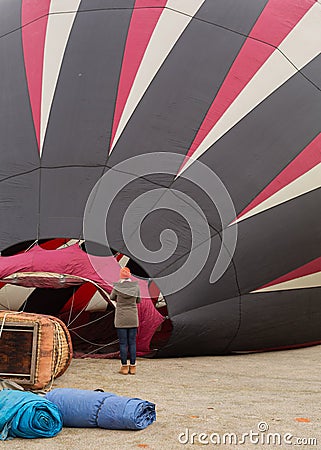 A woman in warm winter clothes watches as a red white and black hot air balloon fills in preparation for lift off Editorial Stock Photo