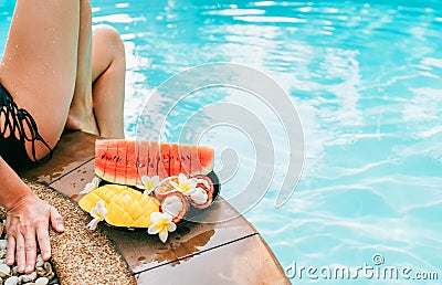 Woman weared swimsuit sitting on swimming pool side with plate of tropical fruits Stock Photo