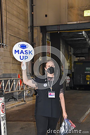 A woman wearing a black face mask is holding a round sign that says mask up outside a Broadway theater Editorial Stock Photo