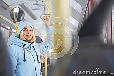 Woman wearing blue cap and winter jacket holding handle enjoying trip in bus. Stock Photo