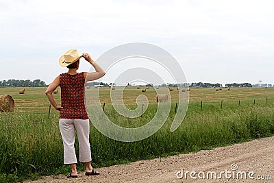 Woman wearing a cowboy hat looking a a field of hay bales. Stock Photo