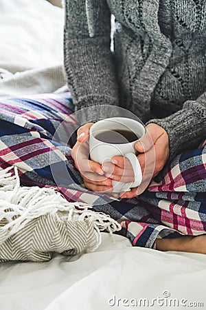 Woman wearing cozy pyjamas and gray cardigan drinking tea on a bed Stock Photo