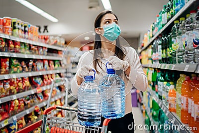 Woman wearing face mask buying bottled water in supermarket/drugstore with sold-out supplies.Prepper buying bulk supplies Stock Photo