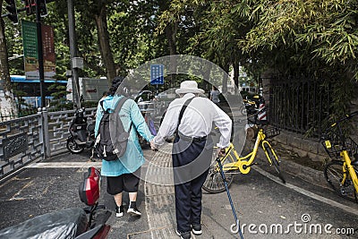 A woman wearing a hat and a walking stick wearing a white coat and a humpbacked elderly woman walking in the street Editorial Stock Photo