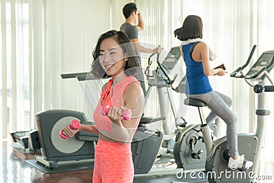 Woman wearing orange sportswear while holding dumbbells. fitness slim young woman lifting weights in gym.Concept of Stock Photo