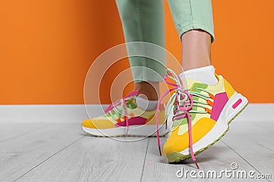 Woman wearing pair of new stylish sneakers near orange wall, closeup. Space for text Stock Photo