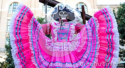 Woman wears sugar skull mask and bright pink Jalisco dress in celebration of Dia de los Muertos / Day of the Dead Editorial Stock Photo