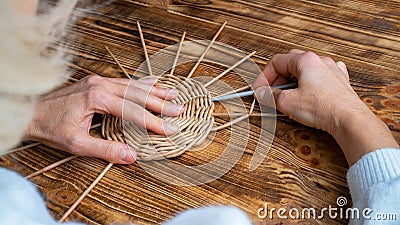 Woman weaves basket of paper tubes on wooden table. Process of weaving a decorative basket from tubes twisted from paper Stock Photo