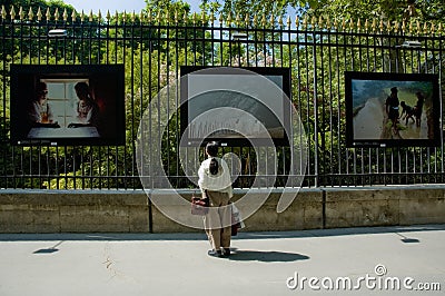 Woman whatching photos exibited on the fence Editorial Stock Photo