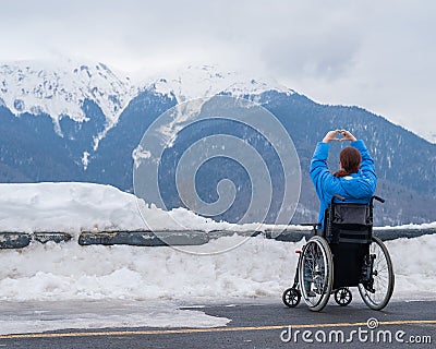 A woman in a wheelchair holds her hands in the shape of a heart in the mountains in winter. Stock Photo