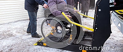 A woman in a wheelchair on a lift of a specialized vehicle for people with disabilities. Taxi for the disabled. Yellow bar and Stock Photo