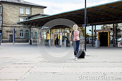 Woman With Wheeled Luggage Walking Outside Train Station Stock Photo