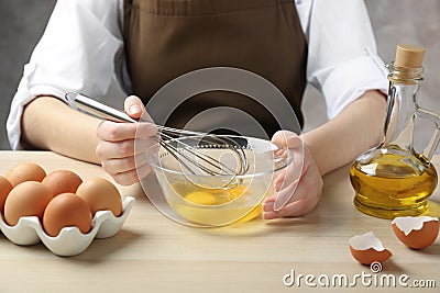Woman whisking eggs in glass bowl at wooden table, closeup Stock Photo