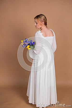 A woman in a white dress stands with her back and holds a bouquet of tulips and irises. March 8. Women's Day. Women's holiday. Mom Stock Photo