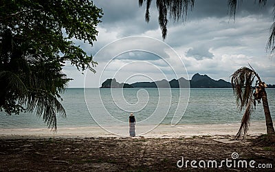Woman in white fedora hat and sarong standing on the beach with islands in the background Stock Photo