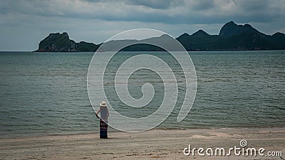 Woman in white fedora hat and sarong standing on the beach with islands in the background Stock Photo