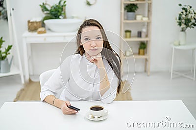 A woman in a white shirt is drinking coffee in a cafe. A female office worker at a lunch break solves a business problem Stock Photo