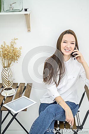 A woman in a white shirt and jeans sits in a cafe and drinks coffee. Female office worker at the lunch break talking on Stock Photo