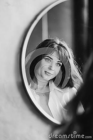 a woman in a white shirt looks at reflection in a round mirror. black and white Stock Photo