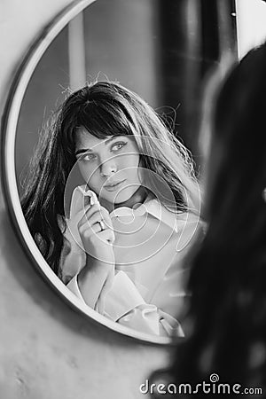 a woman in a white shirt looks at reflection in a round mirror. black and white Stock Photo