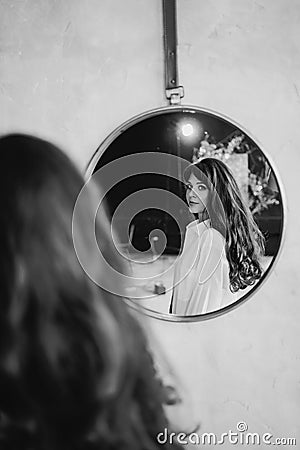 a woman in a white shirt looks at reflection in a round mirror. black and white Stock Photo