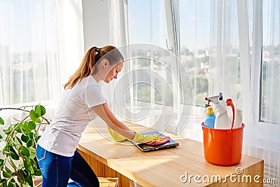 Woman in white shirt and yellow protective rubber gloves cleaning at home and wiping dust with pink rag on laptop computer. Stock Photo