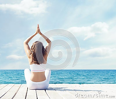 Woman in white sportswear doing yoga on a wooden pier. Sea and sky background. Yoga, sport, vacation and travelin Stock Photo