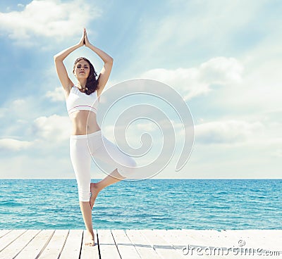 Woman in white sportswear doing yoga on a wooden pier. Sea and Stock Photo