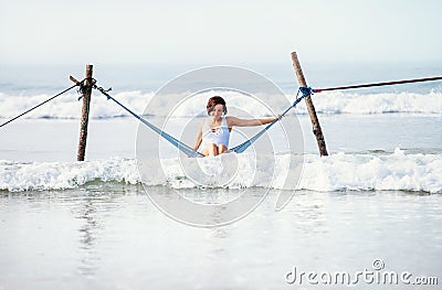 Woman in white swimsuit sits in hammock swing over the ocean surf line Stock Photo