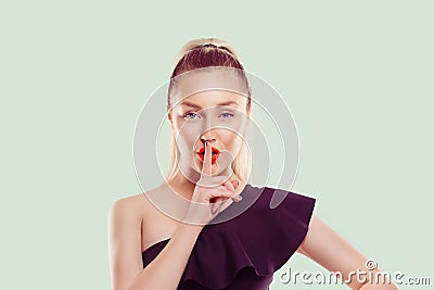 Woman wide eyed asking for silence or secrecy with finger on lips hush hand gesture light green background wall Pretty girl Stock Photo