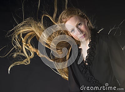 woman wind blowing long blond hair portrait smiling wearing frilly black dress strong black background 55918324
