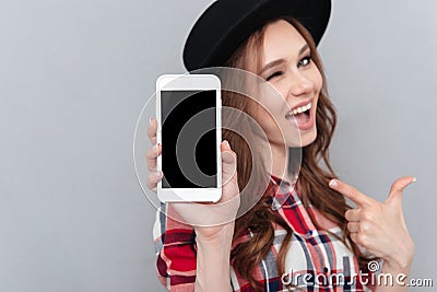 Woman winking and pointing finger at blank mobile phone screen Stock Photo
