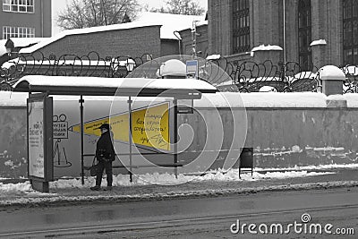 Woman in winter clothes walking alone on a snowy road near bus stop in a little town. Wintertime. Selective focus Editorial Stock Photo