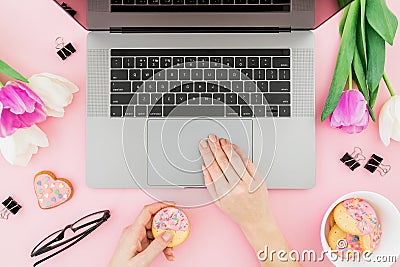 Woman working with computer. Office desk with laptop, tulip flowers, glasses, pen and cookies on pink background. Flat lay. Top vi Stock Photo